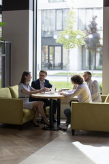Happy young and ambitious businesspeople sit at table in modern office laughing, brainstorm, discuss business ideas together, smiling colleagues having fun, joke, negotiating at team briefing indoors