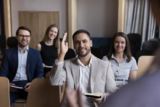 Businessman take part in educational, motivational training event seated with colleagues attend together in seminar, raises his arm for ask question, participate in voting, having opinion to share it