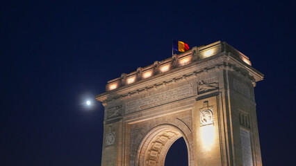 Fototapeta premium Arch of Triumph in Bucharest. Night landscape under the full moon with this iconic landmark from Romania. Long exposure photo.
