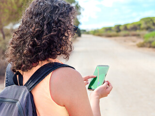 Woman's back with gps location on a cell phone while walking or hiking in the mountains or forest.