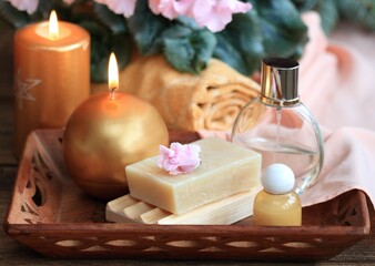 Spa concept with candles in gold and pink. Handmade olive soap, facecloth, towel, candles and pink cyclamen on wooden table. - obrazy, fototapety, plakaty