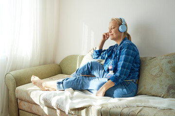 Fototapeta premium Mature woman in blue headphones relaxing on the couch listening to music