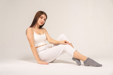 Fototapeta na wymiar Cute young brown-haired girl in a white top and knitted trousers posing while sitting on a white background
