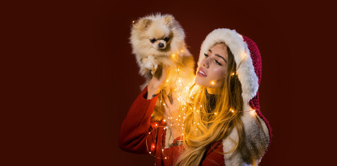 Portrait of a young woman celebrate winter Christmas holidays hold puppy dog on red background.