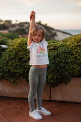 Beautiful little girl child in fashionable summer clothes with a white T-shirt, green leggings and...