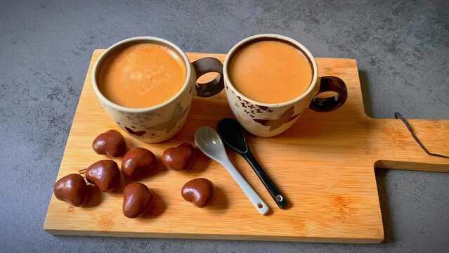 Deux tasses du caf&eacute;  avec cuill&egrave;res et chocolats en forme coeur sur un support bout du bois. Petit d&eacute;jeuner romantique Saint Valentin mariage d&eacute;claration d'amour caf&eacute; avec du chocolat 