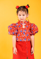 Happy Asian Chinese little girl smile wearing red cheongsam, Portrait children in traditional dress with greeting gesture celebration for Chinese New Year, studio short isolated on yellow background