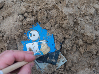 carefully digging floppy floppy disks out of the sand with the help of archaeological tools.