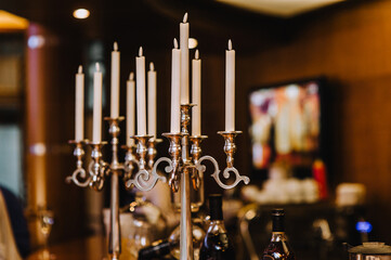An antique bronze candlestick with burning candles stands on a table indoors.