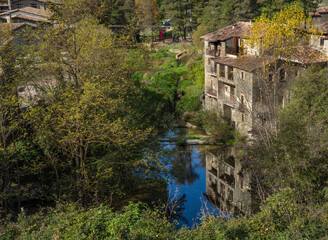 Fototapeta na wymiar View of a medieval house in an old town in Catalonia with the river below reflecting the house surrounded by vegetation