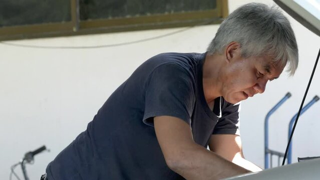 A middle-aged mechanic is repairing inside the engine compartment.