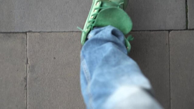 Close up shot of man's lags walking on the pavement street wearing green shoes and jeans. 