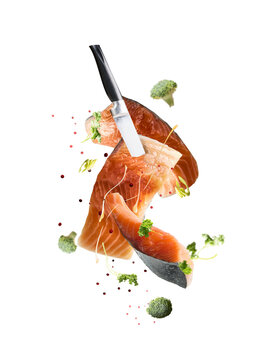 Isolated of flying raw salmon fillets with knife and falling herbs and spices 