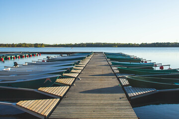 There are many rowboats at the pier.Sunset in the background. There is a calm on the lake