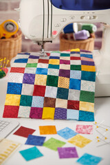Colorful detail of quilt sewn from square pieces on sewing machine, quilting and sewing accessories