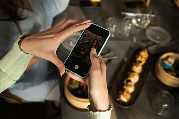 A food blogger photographs Asian dishes with her mobile phone while framing a plate of steamed dim sum for her social networks - food and drink and technology lifestyle concept