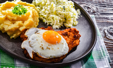 Breaded chicken cutlet with fried egg, potatoes and cabbage