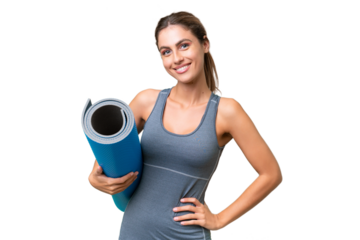 Pretty Young Uruguayan sport woman going to yoga classes while holding a mat over isolated background posing with arms at hip and smiling