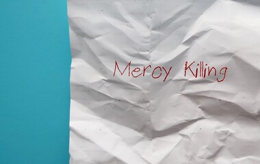 Crumpled paper onblue background with text MERCY KILLING, or EUTHANASIA, an act or practice of persons suffering from painful and incurable disease   ending life to relieve pain and suffering
