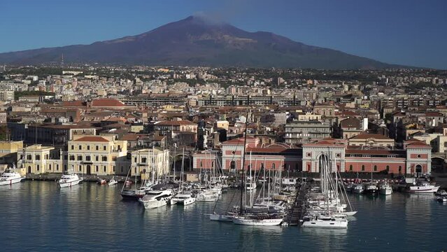 Port of Catania. Volcano Etna with white smoke and blue sky on background. Sicily, Italy