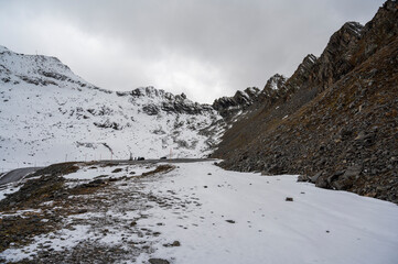 Stone mountain ridge, partially covered with snow, with asphalt road and parking lot below.