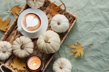 White pumpkins, coffee and autumn leaves on a wicker tray.