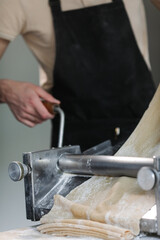 Men's hands turn a mill for thin dumpling dough.