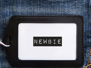 Black corporate ID card on jeans background with text label NEWBIE, refers to inexperienced newcomer wirker employee in the workplace,one who has just started doing activity or first jobber - obrazy, fototapety, plakaty