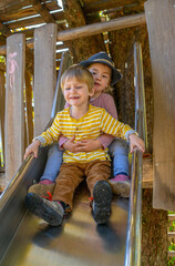 Boy and girl sitting on top on a slide smiling into camera
