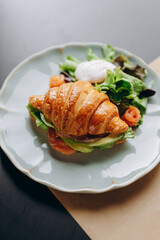 Croissant with avocado and salmon and lettuce and poached egg.