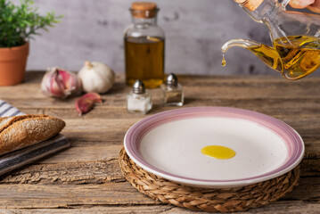Extra virgin olive oil pouring from an oil can into a round white plate, on a rustic wooden table,...