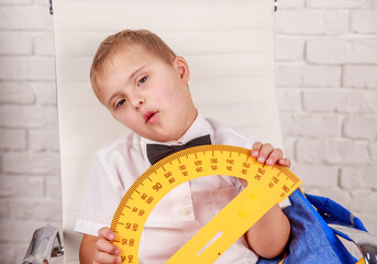 Happy boy with down syndrome holds a protractor ruler in his hands, early development, preparation...