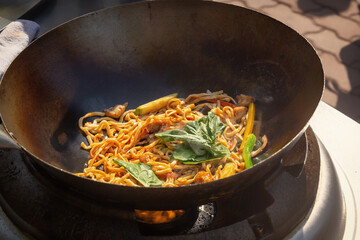 Cooking noodles with meat and vegetables in a deep wok over an open fire. street food