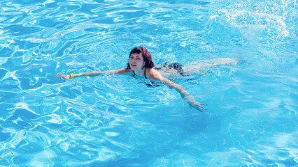 Fototapeta na wymiar Young brunette woman swims blue water of the pool.