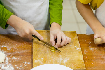 Cropped children's hands with knife cut vegetables on wooden cutting board. Culinary training.