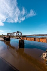 Vertical view of a rusty bridge connecting the riverbanks under the blue sky