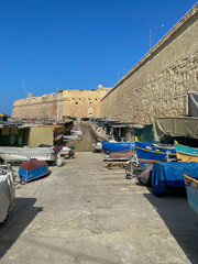 Fototapeta na wymiar Boats on drylands at a small boatyard with huts alongside the walls of Fort Saint Elmo, a star fort in use from 1552 to 1972.- Valletta, Malta.