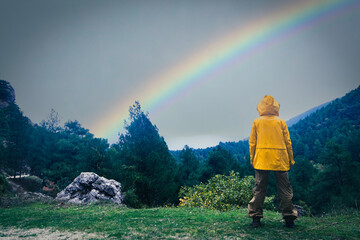 girl on the top of mountain with yellow coat watching rainbow