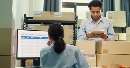 Asian business partner man hold tablet and girl partner wear formal shirt sit front desk computer meeting discuss inventory stock online data in delivery at warehouse. Startup small business concept.