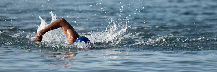 Professional triathlete swimming in ocean open water, male triathlon swimmer swimming in...