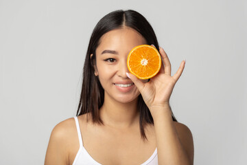 Vitamin C cosmetics concept. Beautiful Asian young woman with clean fresh skin holding orange halves. Facial treatment or female beauty face care concept. Cosmetology, beauty and Spa background