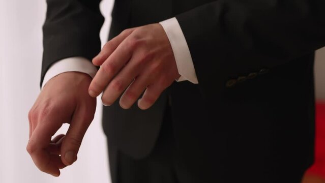 A man in a black suit adjusts the cufflinks of a white shirt