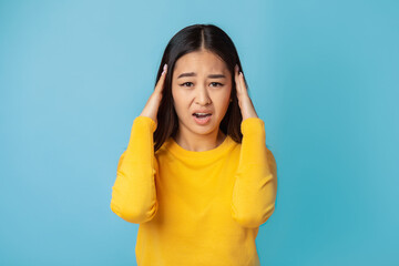 Tired young Asian woman having headache feeling sick, pain, depression, overwork concept. Female holding her head looking at the camera and screaming standing on a pink background