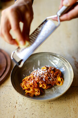 Chef rubs parmesan into a dish of pasta with bolognese sauce