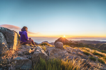 Sitzende Frau, die den Sonnenaufgang über der wunderschönen Berglandschaft von Pico do Ariero beobachtet. Pico do Arieiro, Insel Madeira, Portugal, Europa.