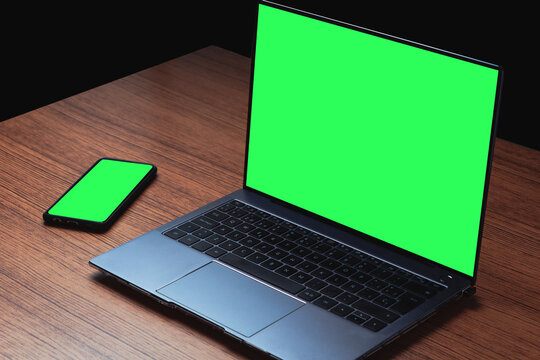 Mockup image with green screen on computer and smartphone on wood desk. Background for advertising text. Space for design.