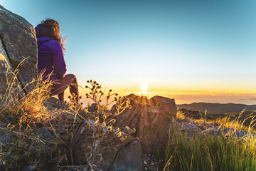 Sitting woman watching the sunrise over the beautiful mountain landscape of Pico do Ariero. Pico do...