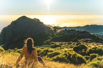 Woman sitting on a mountain meadow enjoying the beautiful mountain landscape of Pico do Ariero at...