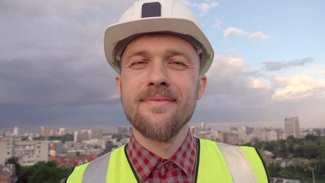 Video call concept: an engineer in white helmet and yellow reflective vest showing agree emotion nodding. A builder wearing hardhat having a video conference inspecting construction site. 4k footage