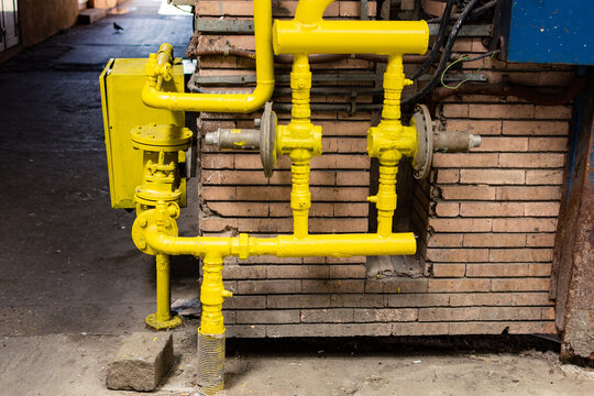 Yellow pipe or plumbing for gas with pressure regulators, valve and a meter locked in a box, next to a brick wall